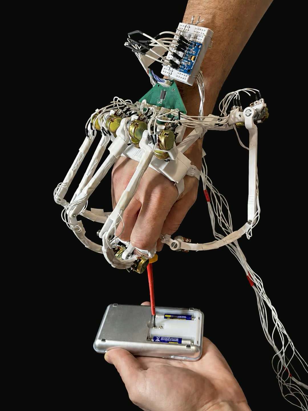 The glove worn on a hand driving a screwdriver into a device: rotary potentiometers at the finger joints and thumb linkage, with the wrist-mounted board behind